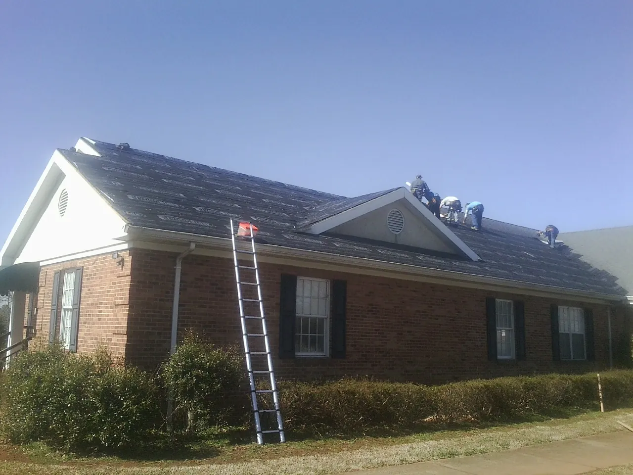 Crew tearing shingles off a brick ranch roof with a ladder set — Emergency Roof Repair work by our crew in Loma Mar