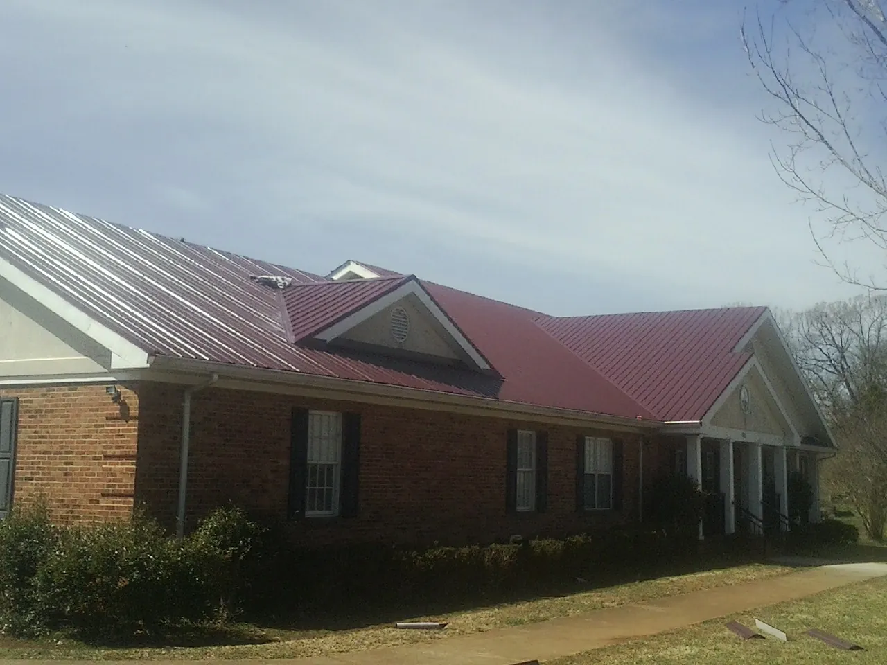 Red metal roof with gabled entries on a long brick building, from a Hail Damage Roof Repair job in Loma Mar
