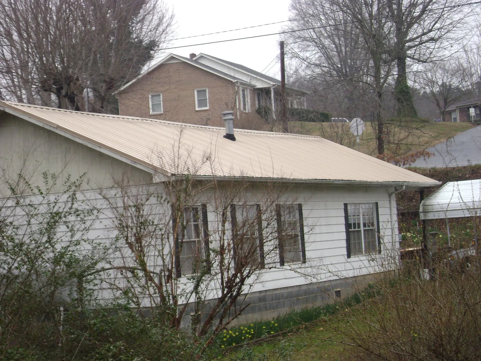Tan metal roof on a white sided house set into a hillside — Commercial Roofing by Roofing Brothers in Loma Mar